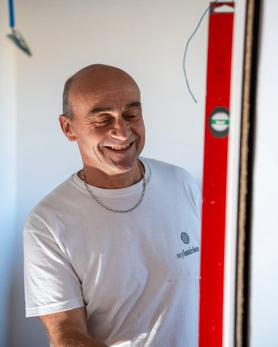 Artisan souriant sur le chantier, à côté d’un grand niveau à bulle rouge