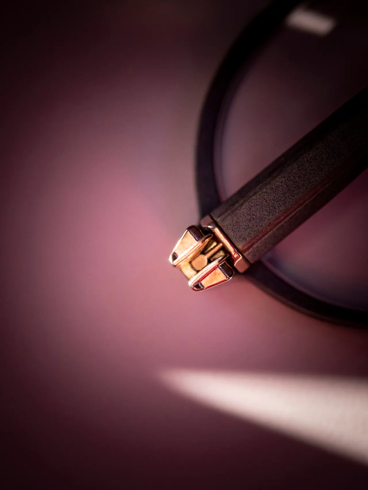 Détail d’une monture : charnière en or rose et branche noire, sous une lumière rasante