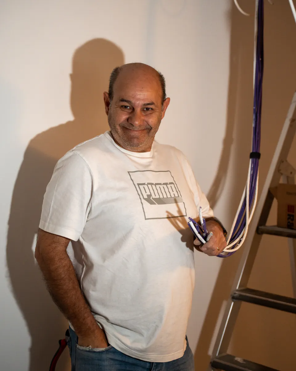 Électricité : un artisan souriant, une poignée de câbles à la main, au pied d’un escabeau