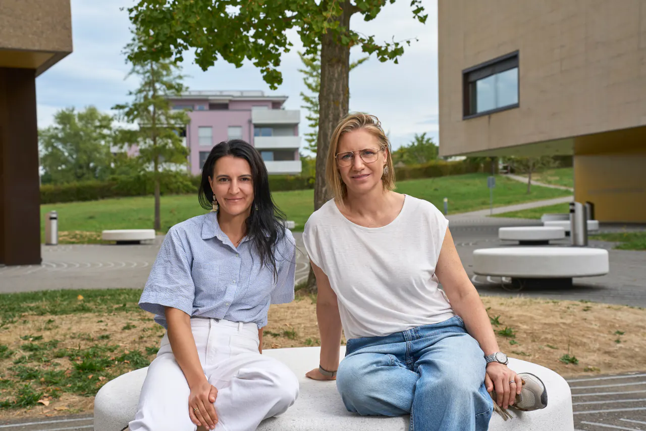 Florence Tuccinardi et Valérie Blanchard, fondatrices de Voilà — Vision-Optométrie à Payerne, assises côte à côte sur un banc en extérieur