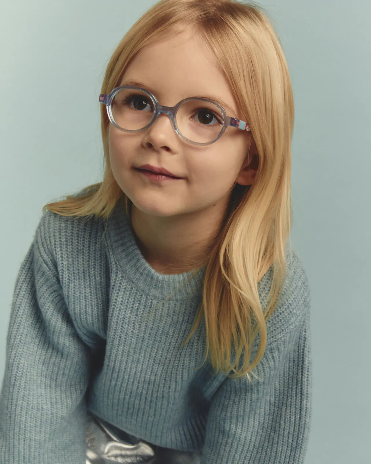 Fillette portant des lunettes rondes bleu translucide à paillettes et un pull en maille bleu, modèle La Reine des Neiges de la collection enfant Disney