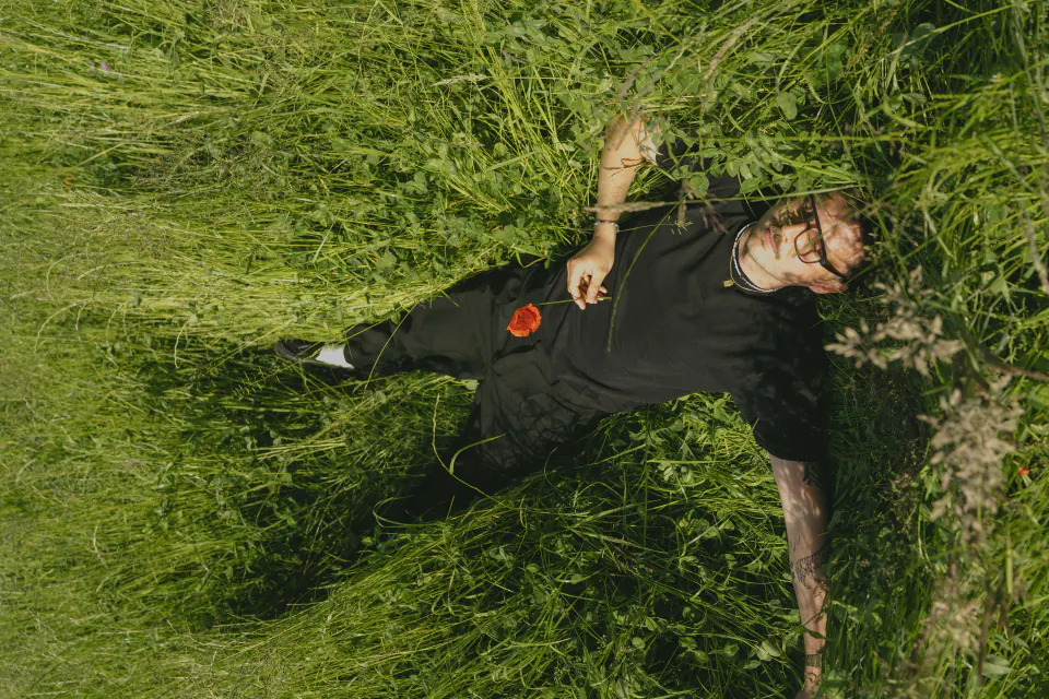 Monture Lars LACET portée allongé dans une prairie, un coquelicot à la main