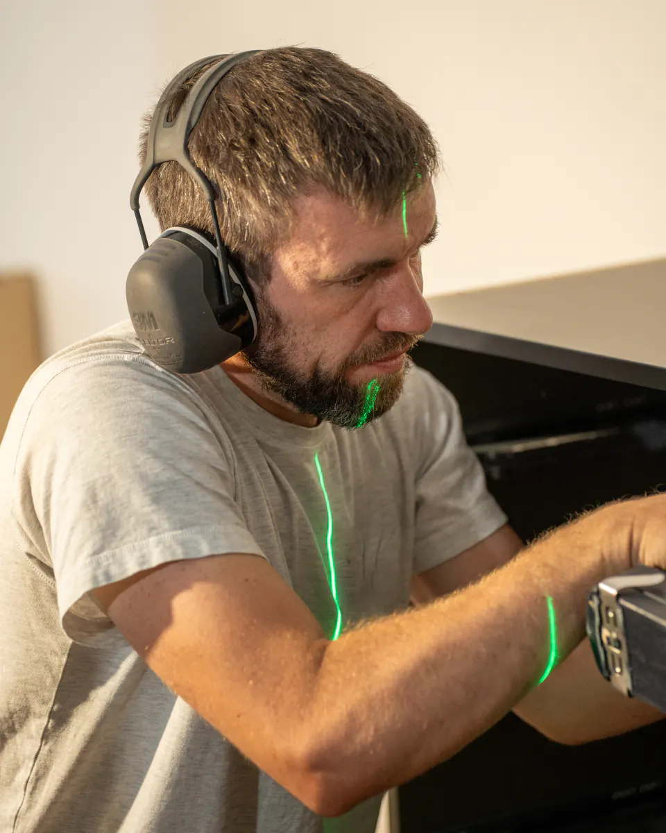 Menuisier concentré, casque antibruit sur les oreilles, traversé par la ligne verte d’un niveau laser